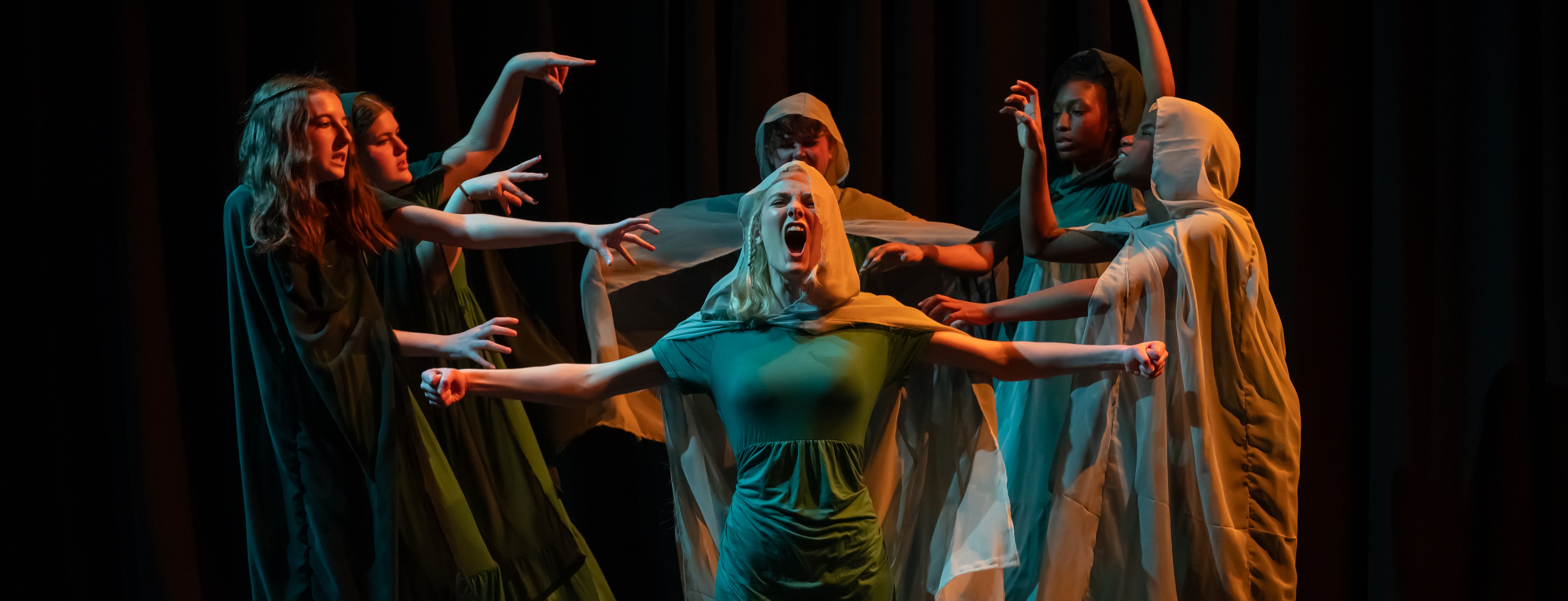 A young person roars with a wide open mouth, surrounded by other young women.